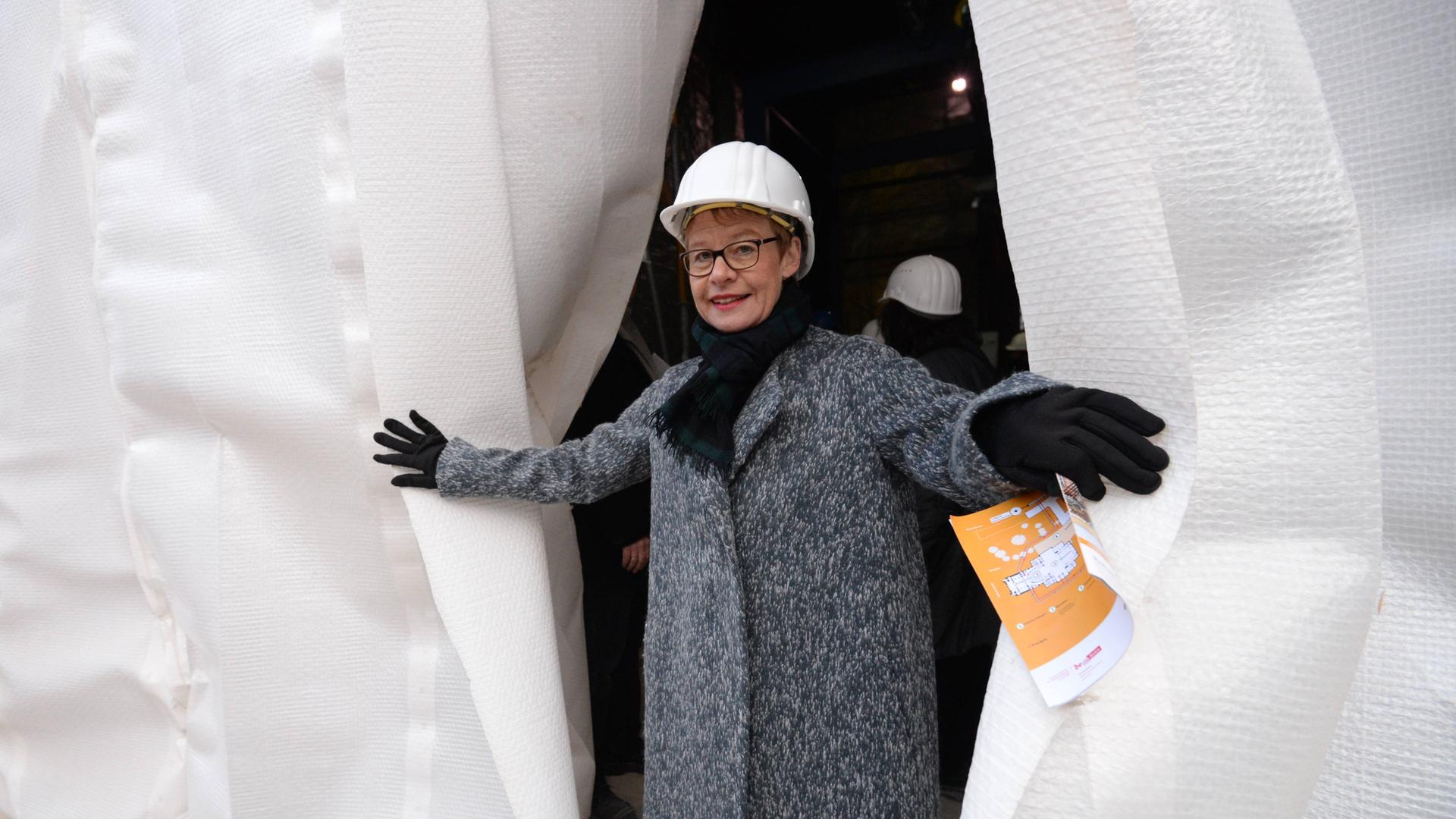 Die ehemalige Senatsbaudirektorin Regula Lüscher mit Bauarbeiterhelm schaut hinter einem Vorhang hervor anläßlich des Beginns der Sanierung der Staatsoper Unter den Linden im Dezember 2014.