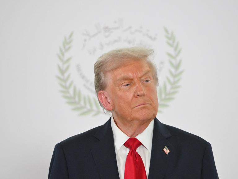 US-Präsident Donald Trump posiert beim Gaza-Friedensgipfel in Scharm el-Scheich für ein Foto. Im Hintergrund ist das Logo des Gipfels zu sehen, das seinen Kopf umrahmt.