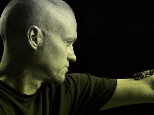 Porträt von Tim Friede, um dessen ausgestreckten Arm sich eine Wasserkobra schlängelt.