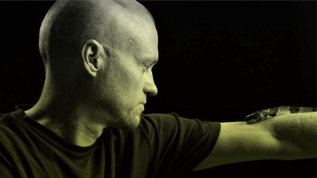 Porträt von Tim Friede, um dessen ausgestreckten Arm sich eine Wasserkobra schlängelt.