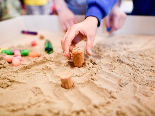 Eine Kinderhand greift nach einem Korken, der in einem Sandkasten steckt. Es handelt sich um den ersten Inklusionsspielplatz für Schulkinder. Eine Kinderhand greift nach einem Korken, der in einem Sandkasten steckt. Es handelt sich um den ersten Inklusionsspielplatz für Schulkinder.