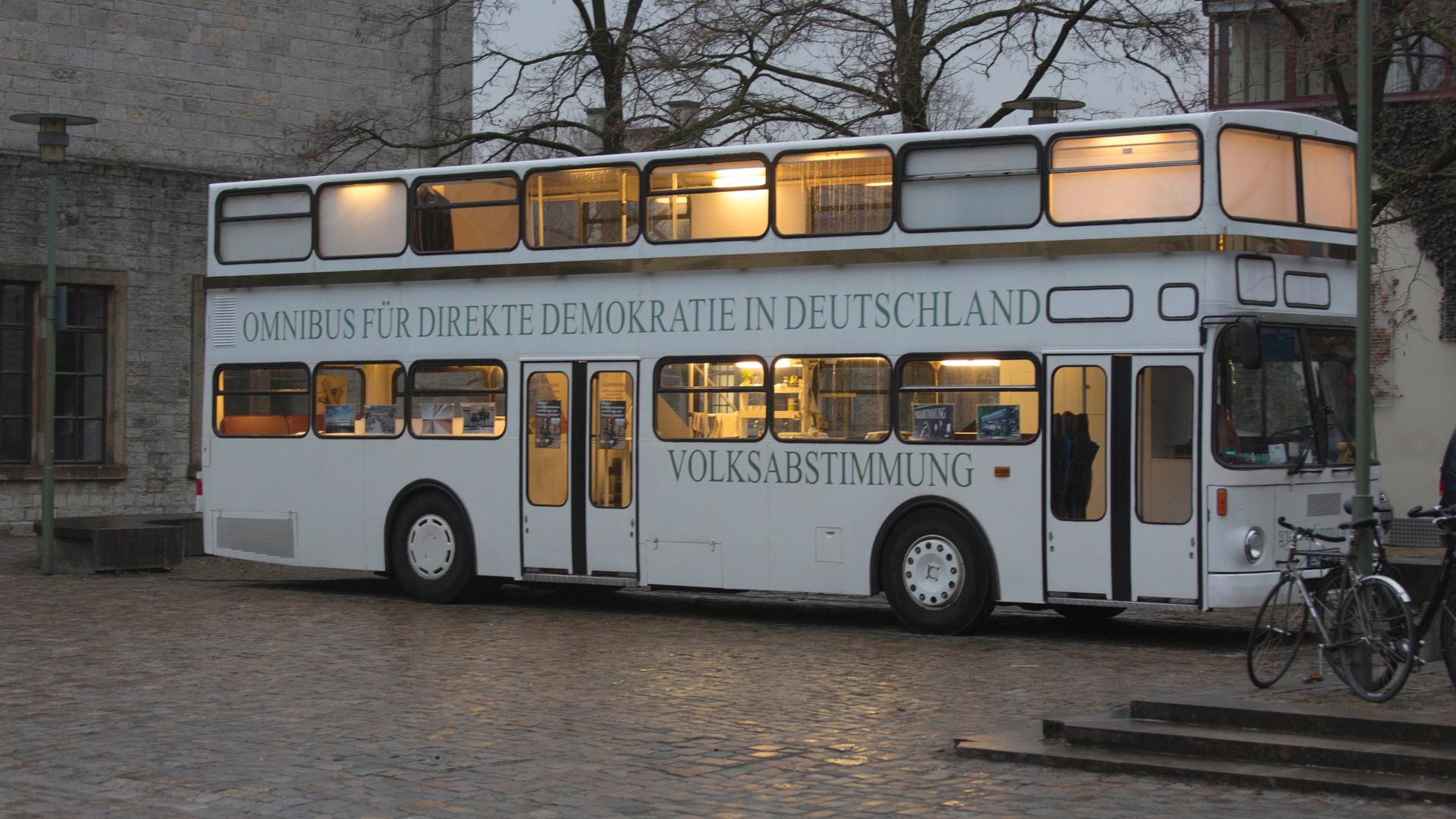 Der sogenannte "Omnibus für direkte Demokratie in Deutschland" einer Bürgerinitiative steht auf einem öffentlichen Platz. Es herrscht Dämmerlicht und der Bus ist innen beleuchtet. 