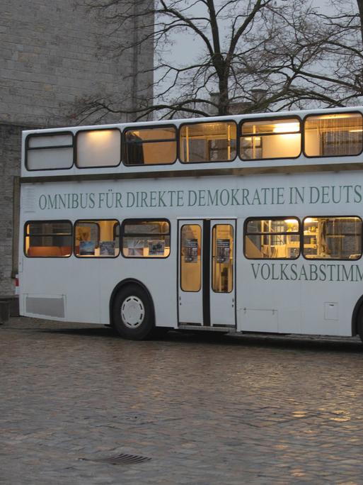 Der sogenannte "Omnibus für direkte Demokratie in Deutschland" einer Bürgerinitiative steht auf einem öffentlichen Platz. Es herrscht Dämmerlicht und der Bus ist innen beleuchtet. 