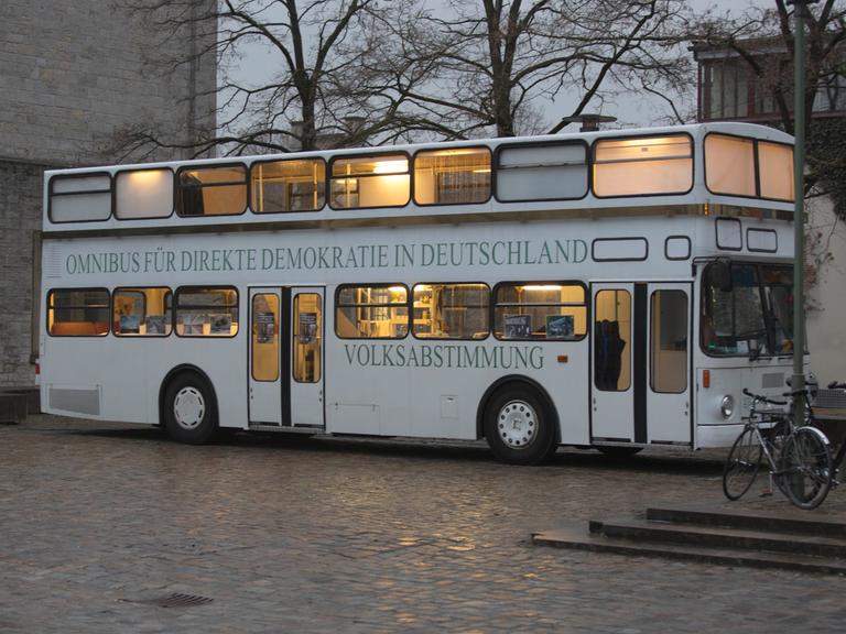 Der sogenannte "Omnibus für direkte Demokratie in Deutschland" einer Bürgerinitiative steht auf einem öffentlichen Platz. Es herrscht Dämmerlicht und der Bus ist innen beleuchtet. 