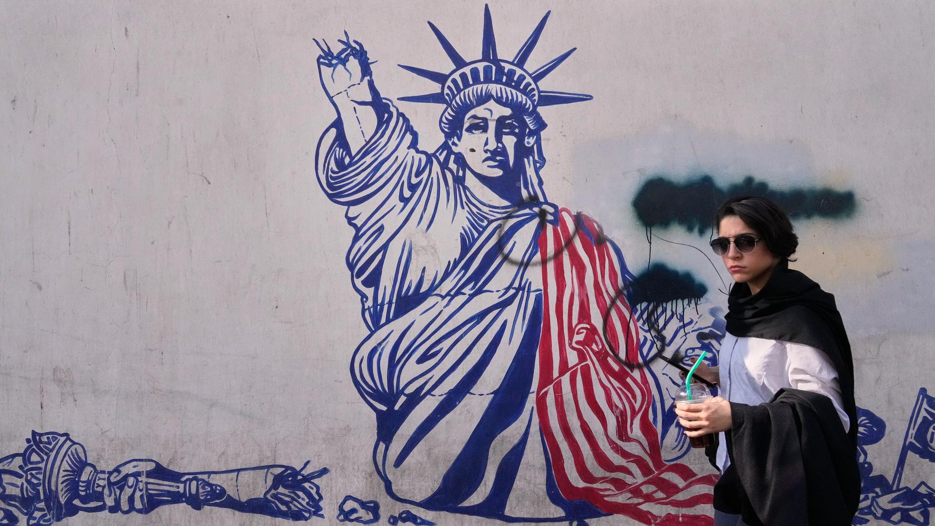 Wandbild an der früheren US-Botschaft in Teheran zeigt die Freiheitsstatue mit abgeschlagenem Arm. Davor geht eine Frau spazieren. Wandbild an der früheren US-Botschaft in Teheran zeigt die Freiheitsstatue mit abgeschlagenem Arm. Davor geht eine Frau spazieren.