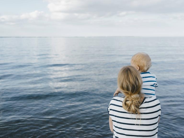 Eine Mutter steht mit ihrem jungen Sohn am Meer.