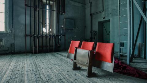 Drei Zuschauerstühle stehen hinter der Bühne eines verlassenen Theaters.