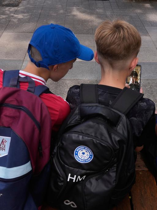 Drei Elfjährige benutzen ihre Handys, man sieht die Jungen von hinten. 