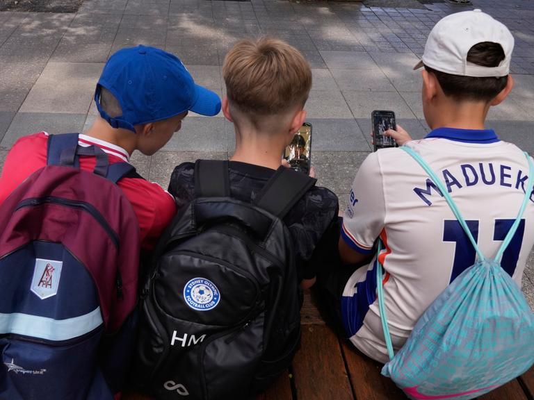 Drei Elfjährige benutzen ihre Handys, man sieht die Jungen von hinten. 