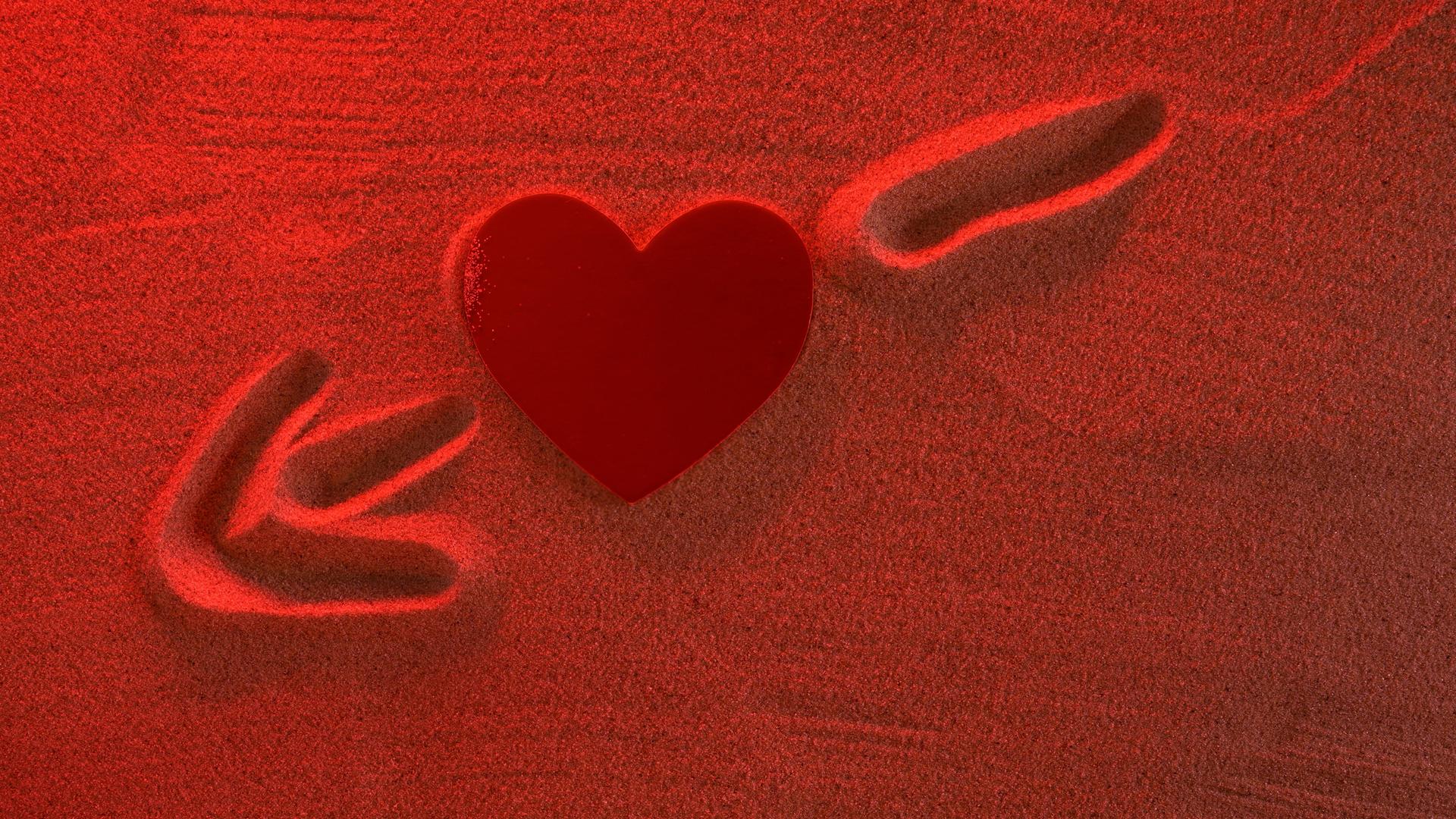 Eine Herzstruktur mit einem Pfeil im Sand. Das Bild ist in rot gehalten.