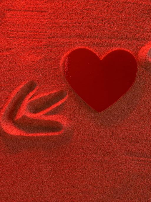 Eine Herzstruktur mit einem Pfeil im Sand. Das Bild ist in rot gehalten.