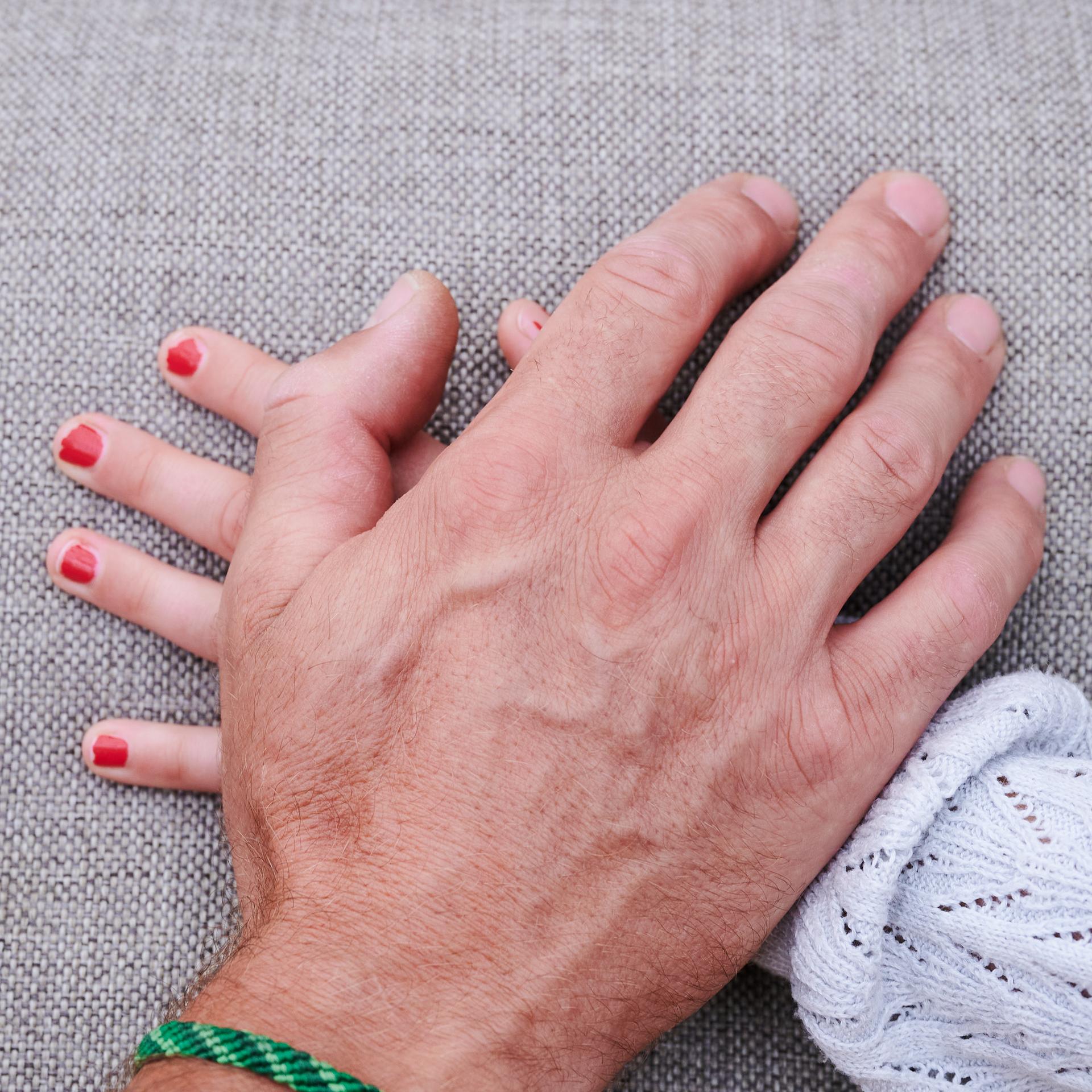 Eine Männerhand liegt auf einer Mädchenhand (gestellte Szene).