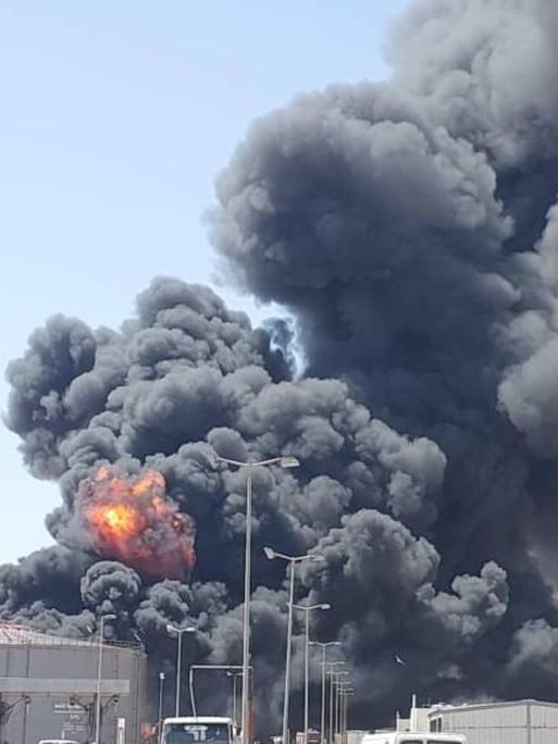 Eine tiefdunkle riesige Rauchwolke steigt über einem Treibstoffdepot auf. An einer Stelle ist in dem Rauch auch Feuer zu erkennen.