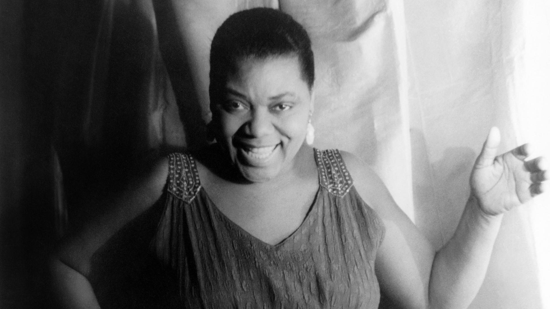 Die afroamerikanische Bluessängerin Bessie Smith in einem schwarzweißen Porträtm am 3. Februar 1936. Die Sängerin trägt ein langes Kleid, kurze Haare und lächelt.