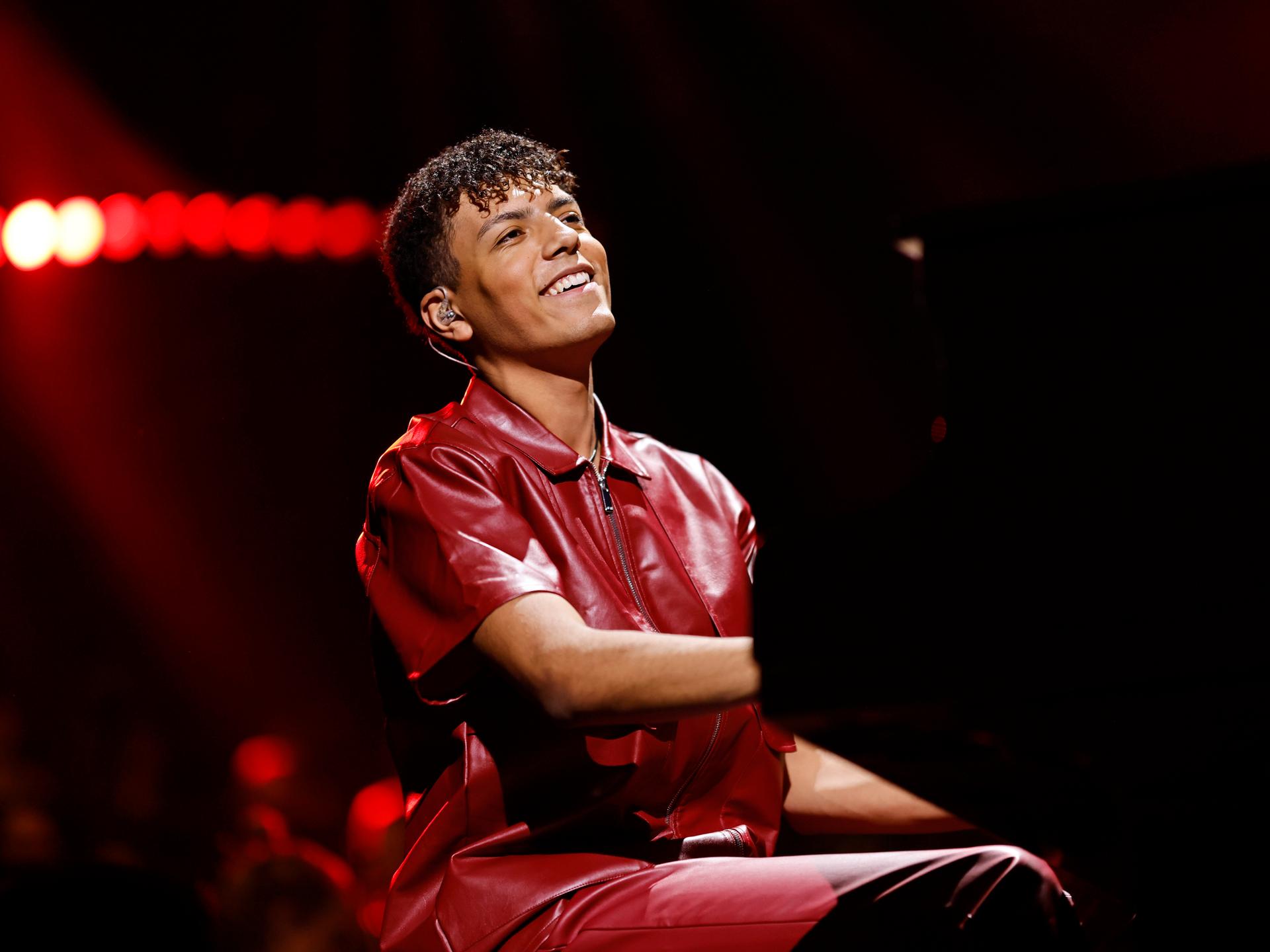 Louis Philippson sitzt bei einem Auftritt lächelnd am Klavier. Er hat dunkles, gelocktes Haar und trägt ein burgunderrotes Lederhemd.