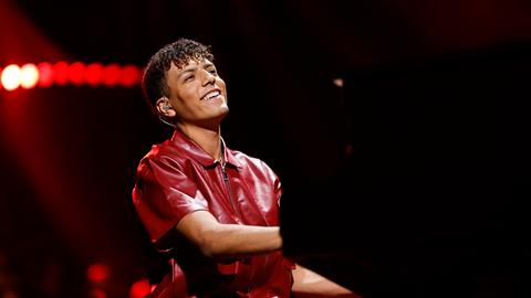 Louis Philippson sitzt bei einem Auftritt lächelnd am Klavier. Er hat dunkles, gelocktes Haar und trägt ein burgunderrotes Lederhemd.