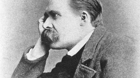 Porträt des Philosophen Friedrich Nietzsche, der seinen Kopf auf seine rechte Hand stützt und grübelnd ins Off des Bildes blickt.