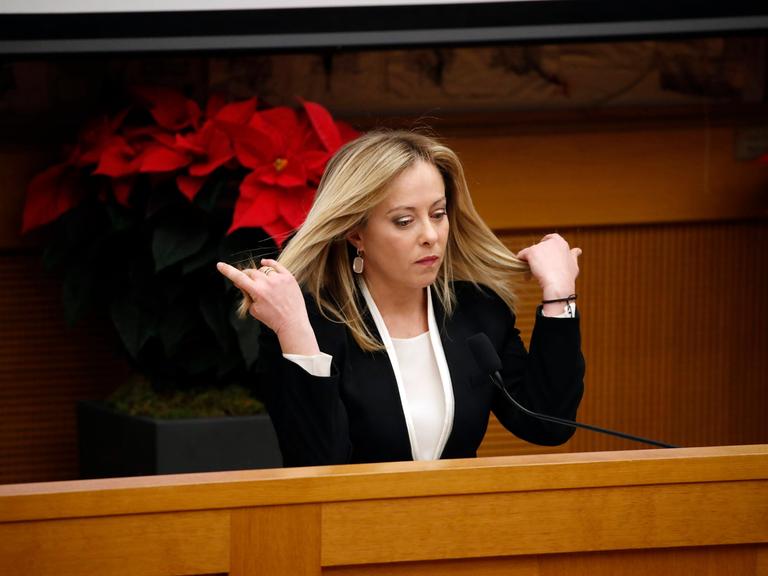 Giorgia Meloni steht an einem Pult im italienischen Parlament und fährt sich mit den Händen durch die langen blonden Haare.