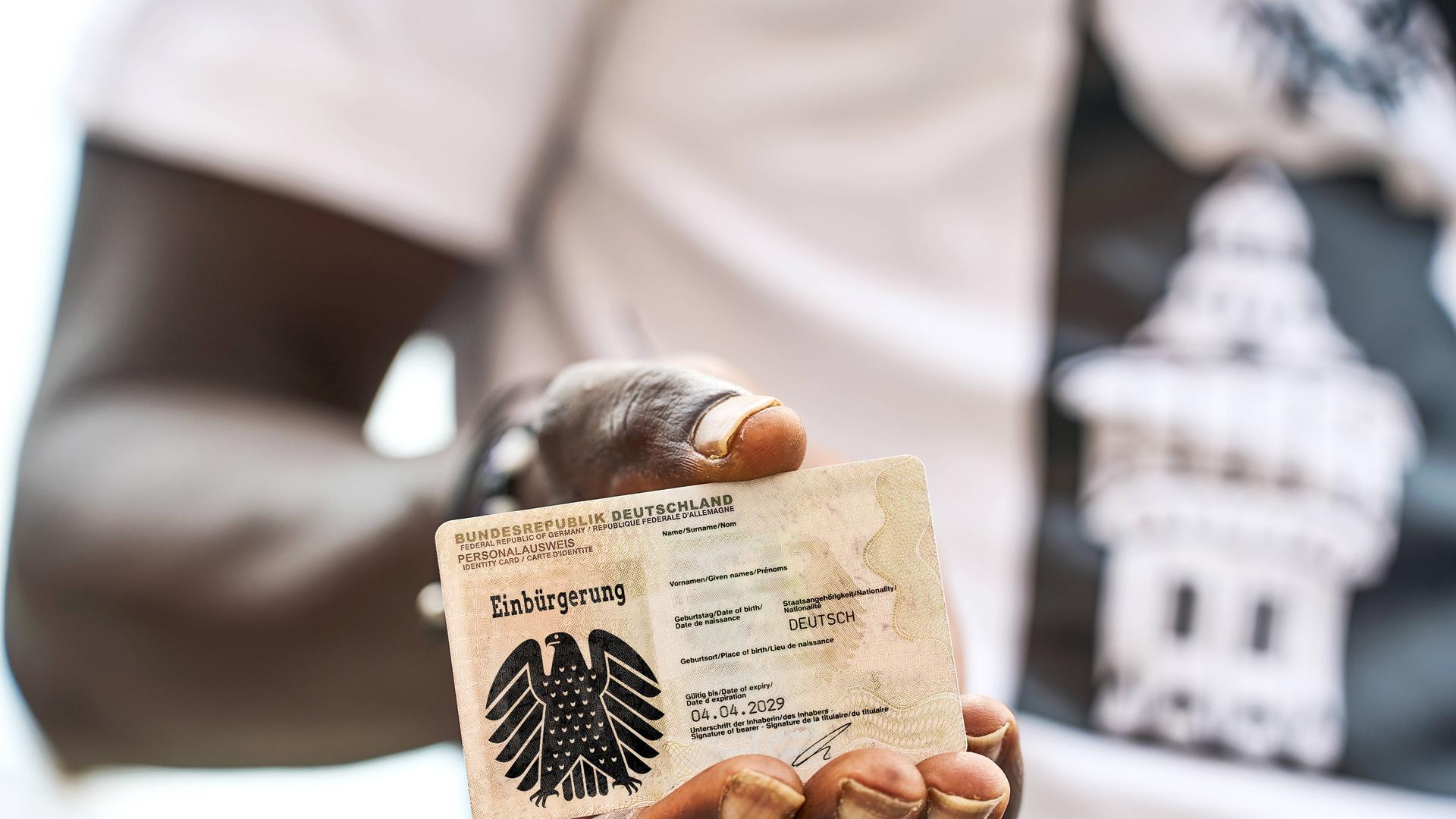 Eine schwarze Hand hält einen deutschen Personalausweis mit Bundesadler und dem Schriftzug: Einbürgerung. (Fotomontage)