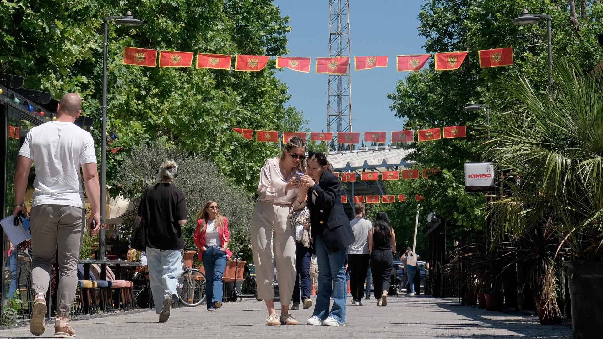 Unter den mit Nationalflaggen geschmückten Straßen der Hauptstadt Podgorica laufen zahlreiche Fußgänger.