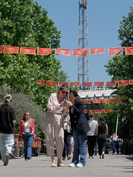 Unter den mit Nationalflaggen geschmückten Straßen der Hauptstadt Podgorica laufen zahlreiche Fußgänger.