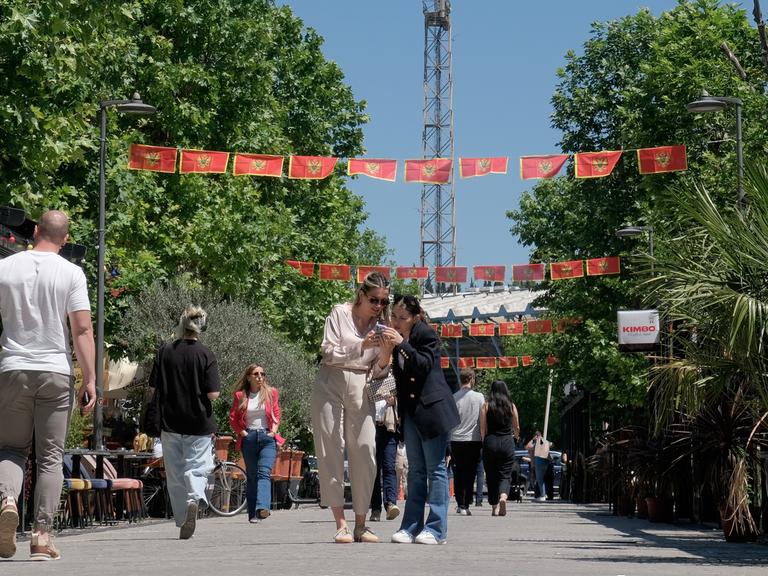 Unter den mit Nationalflaggen geschmückten Straßen der Hauptstadt Podgorica laufen zahlreiche Fußgänger.