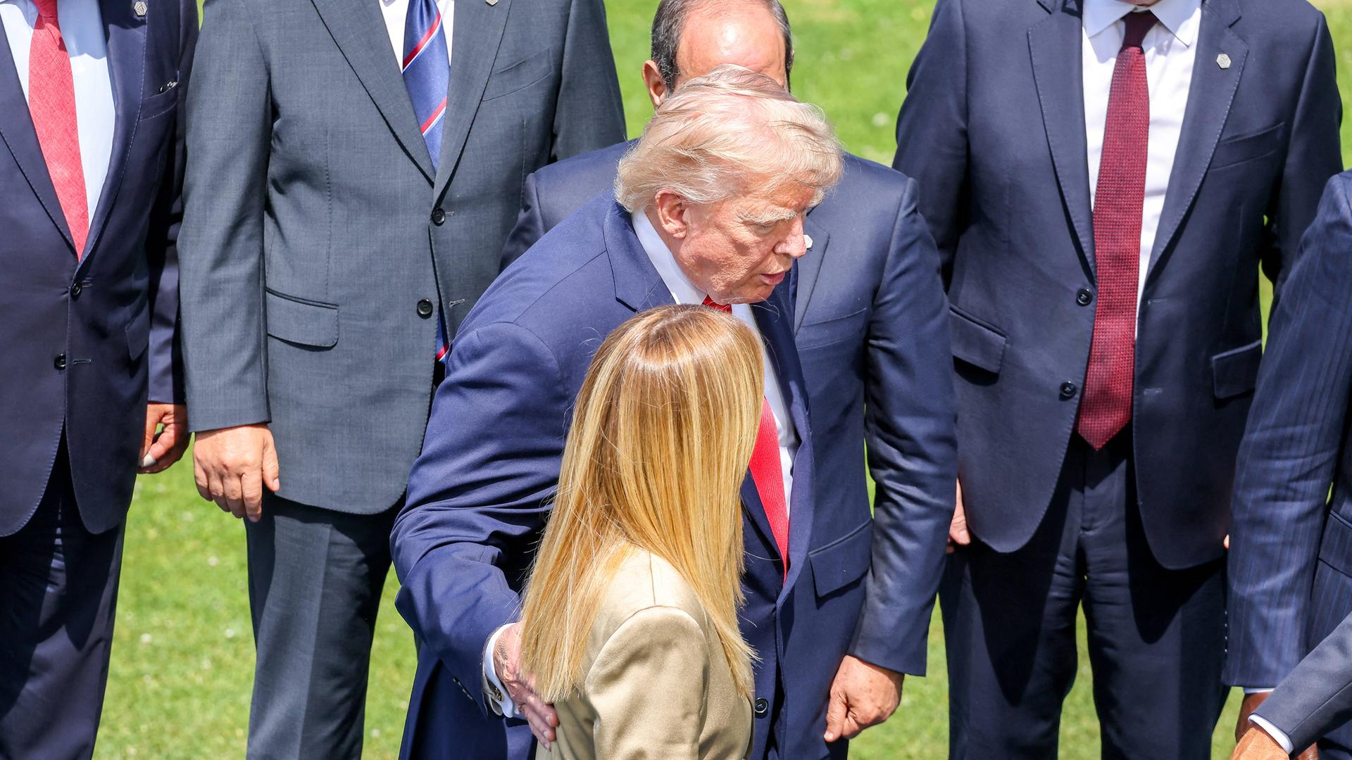Präsident Trump und Ministerpräsidentin Meloni laufen nebeneinander an mehreren Männern in Anzügen vorbei. Er hat eine Hand auf ihren Rücken gelegt. Präsident Trump und Ministerpräsidentin Meloni laufen nebeneinander an mehreren Männern in Anzügen vorbei. Er hat eine Hand auf ihren Rücken gelegt.