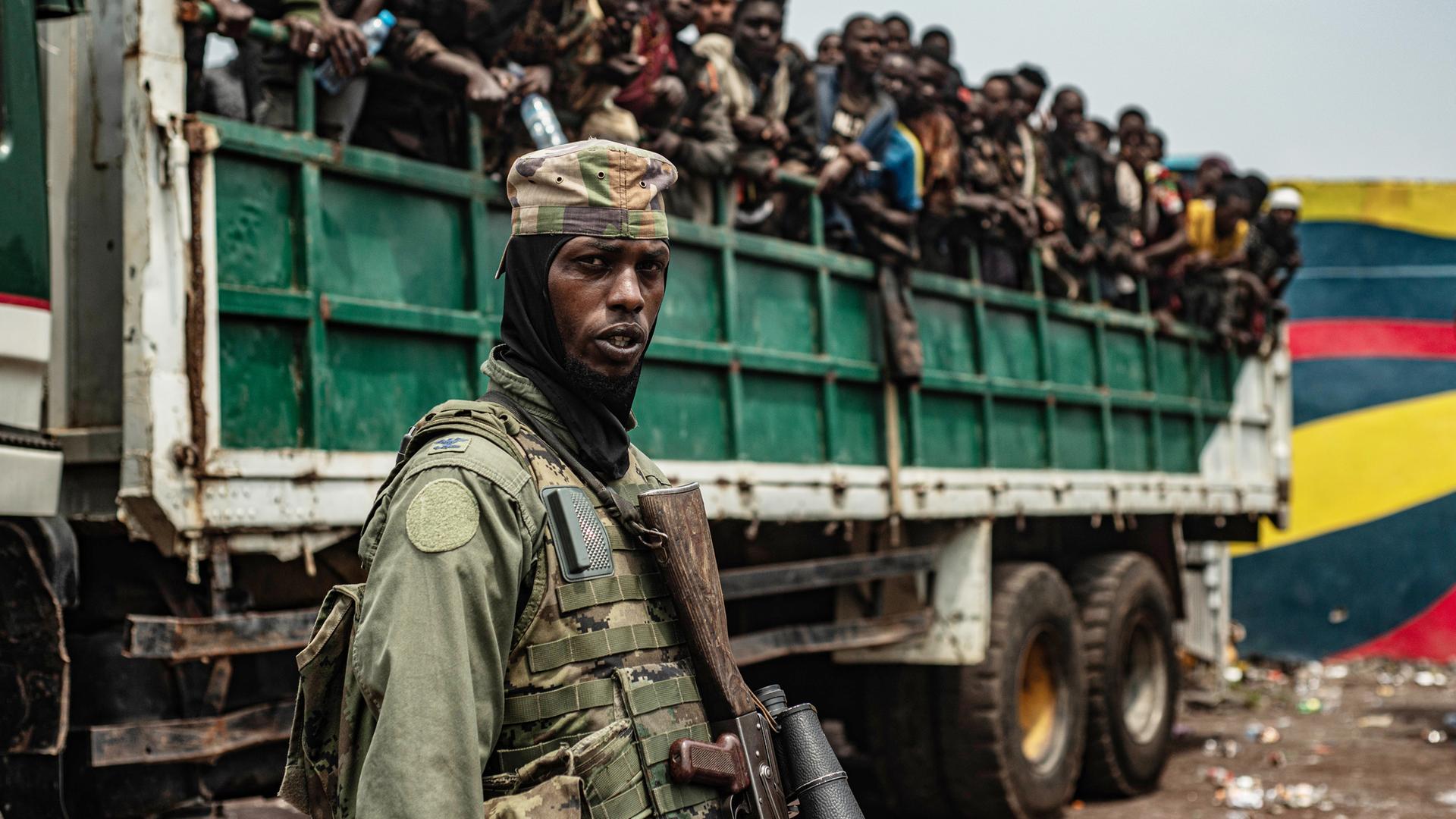 Ein M23-Kämpfer steht im Vordergrund, während inhaftierte FARDC-Soldaten auf Lastwagen verladen werden.