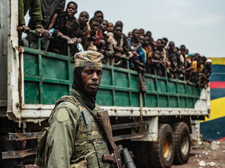 Ein M23-Kämpfer steht im Vordergrund, während inhaftierte FARDC-Soldaten auf Lastwagen verladen werden, um an einen unbekannten Ort gebracht zu werden, 30. Januar 2025.