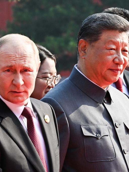 Das Bild zeigt Chinas Staatschef Xi Jinping in einem dunklen Anzug, der der Kleidung von Mao Tsetung nachempfunden ist. Neben ihm steht Russlands Präsident Putin und Machthaber Kim Jong Un aus Nordkorea. 