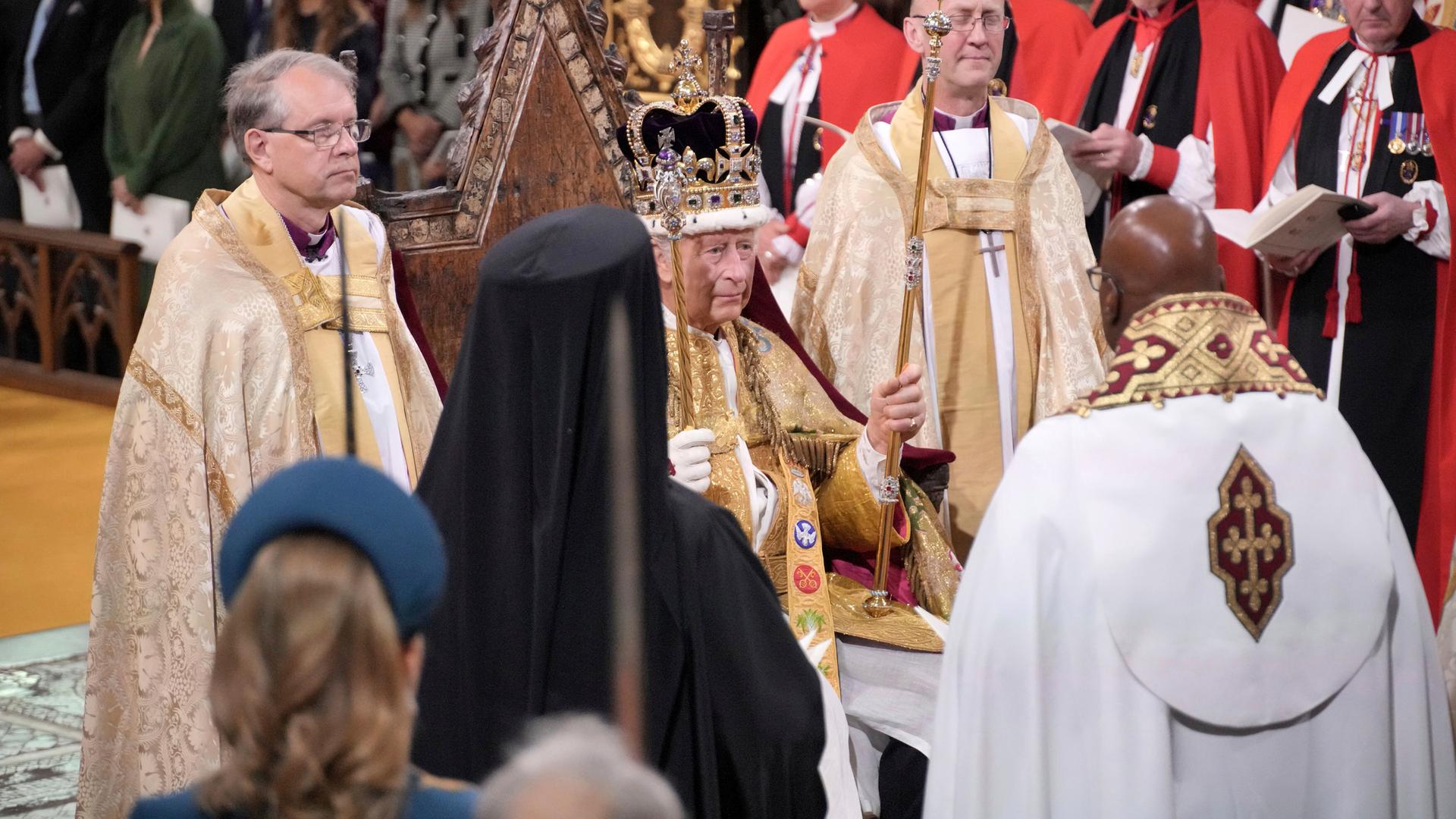 Der frisch gekrönte König Charles III. sitzt in der Westminster Abbey mit der Krone auf dem Haupt, in den Händen hält er das Zepter und den Stab.