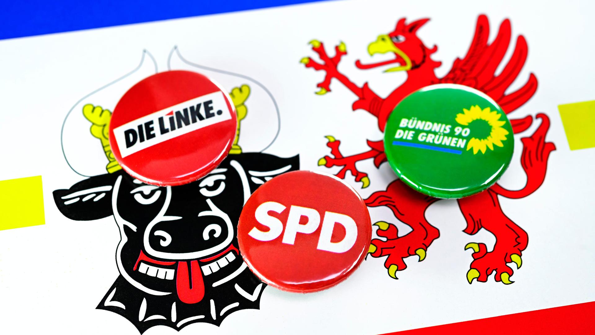 Parteianstecker von SPD, Die Linke und Die Grünen li8egen auf dem Wappen von Mecklenburg-Vorpommern