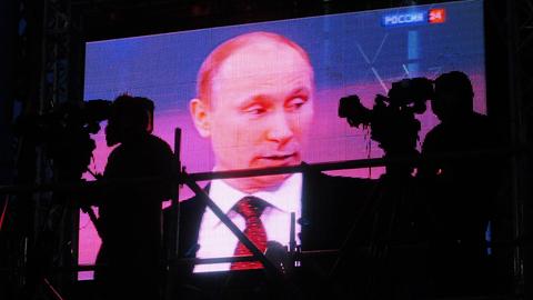Auf einem großen Videobildschirm ist Wladimir Putin während eines Gesprächs zu sehen. Davor sieht man die Silhouetten von zwei Kamerapersonen.