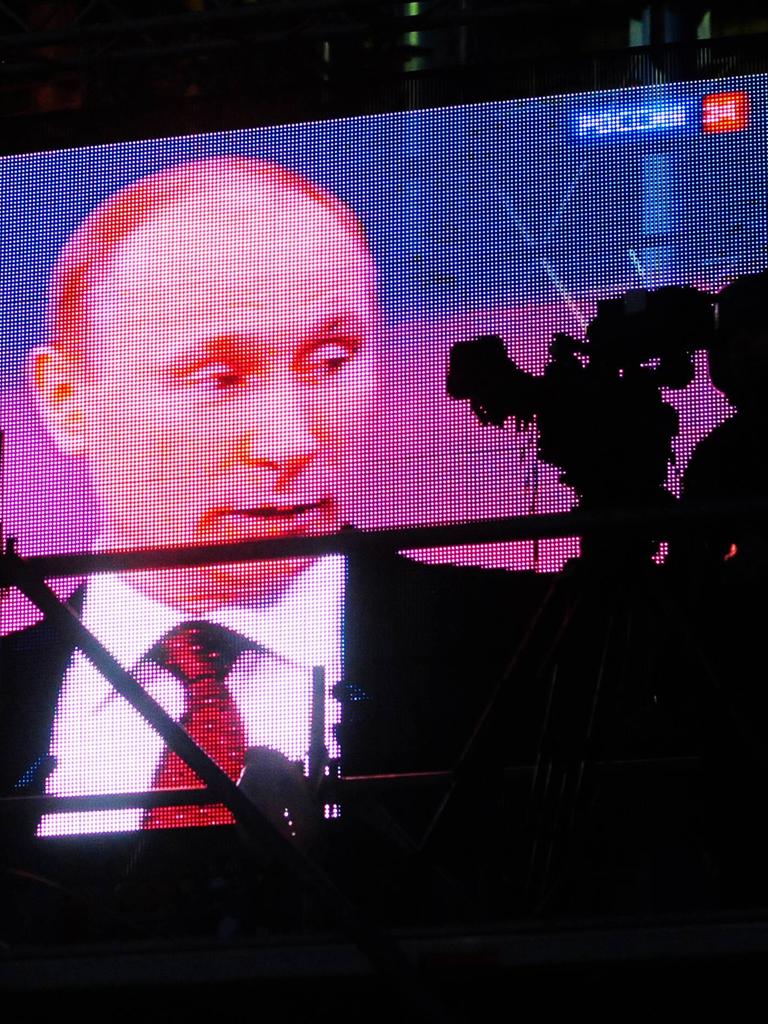 Auf einem großen Videobildschirm ist Wladimir Putin während eines Gesprächs zu sehen. Davor sieht man die Silhouetten von zwei Kamerapersonen.
