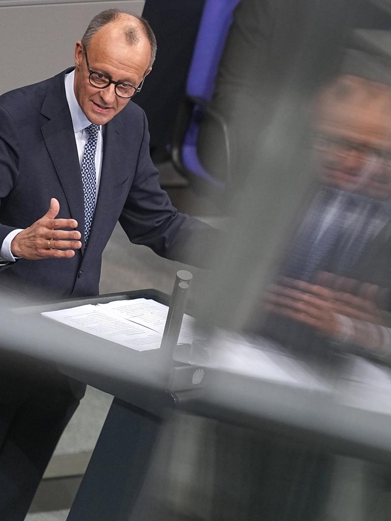 Friedrich Merz, CDU-Vorsitzender und Vorsitzender der CDU/CSU-Bundestagsfraktion, steht im Bundestag am Rednerpult. Er spiegelt sich etwas verschwommen in einer Glasscheibe.