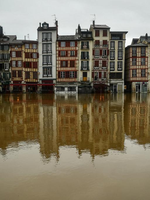 Eine Häuserfront steht infolge einer Überschwemmung im Wasser. Die Gebäude spiegeln sich auf der Wasseroberfläche.