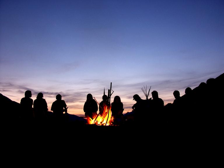 Lagerfeuer mit Menschengruppe als Silhouette in der Dämmerung