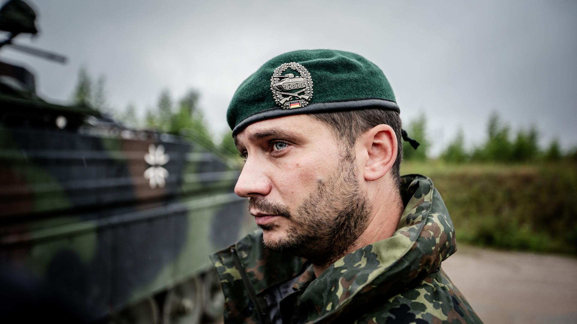 Ein Bundeswehrsoldat in Tarnkleidung und Barett auf dem Kopf steht vor einem Schützenpanzer.