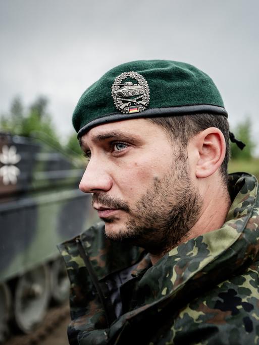 Ein Bundeswehrsoldat in Tarnkleidung und Barett auf dem Kopf steht vor einem Schützenpanzer.
