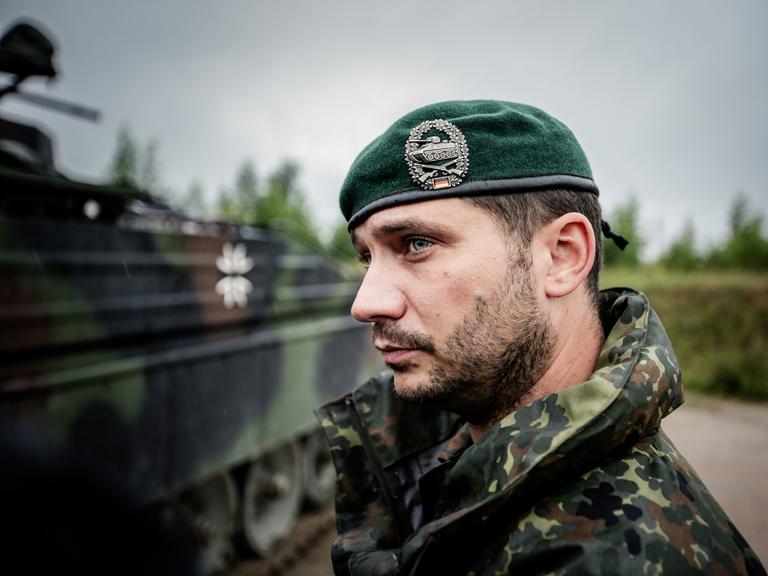 Ein Bundeswehrsoldat in Tarnkleidung und Barett auf dem Kopf steht vor einem Schützenpanzer.