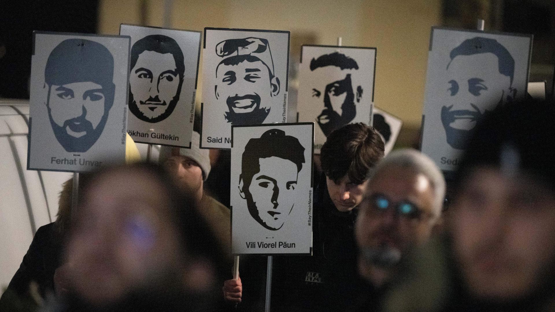 Demonstranten halten Plakate mit stilisierten Bildern der Opfer bei einem Gedenken zum Jahrestag des rassistischen Anschlages von Hanau. Demonstranten halten Plakate mit stilisierten Bildern der Opfer bei einem Gedenken zum Jahrestag des rassistischen Anschlages von Hanau.