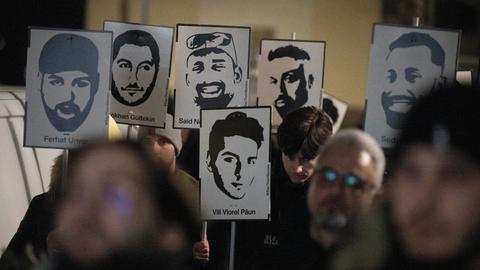 Demonstranten halten Plakate mit stilisierten Bildern der Opfer bei einem Gedenken zum Jahrestag des rassistischen Anschlages von Hanau.