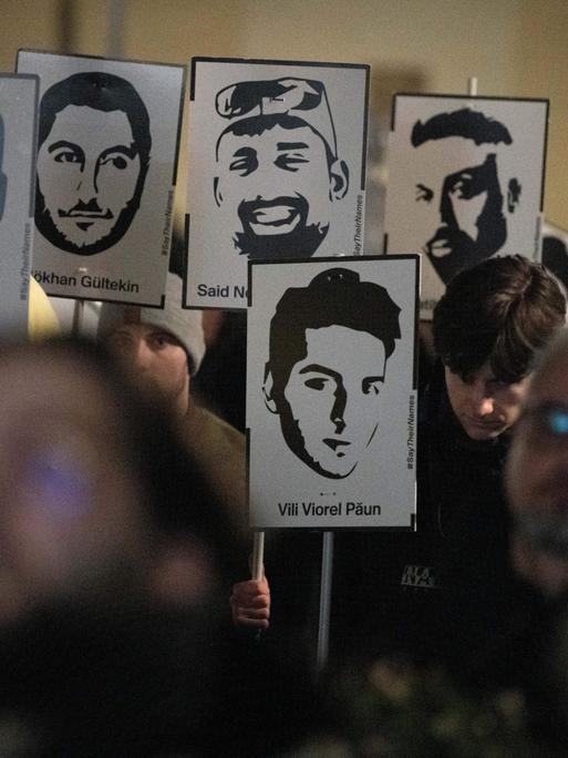 Demonstranten halten Plakate mit stilisierten Bildern der Opfer bei einem Gedenken zum Jahrestag des rassistischen Anschlages von Hanau.