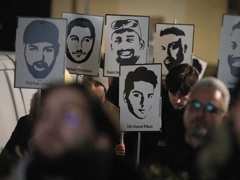 Demonstranten halten Plakate mit stilisierten Bildern der Opfer bei einem Gedenken zum Jahrestag des rassistischen Anschlages von Hanau.