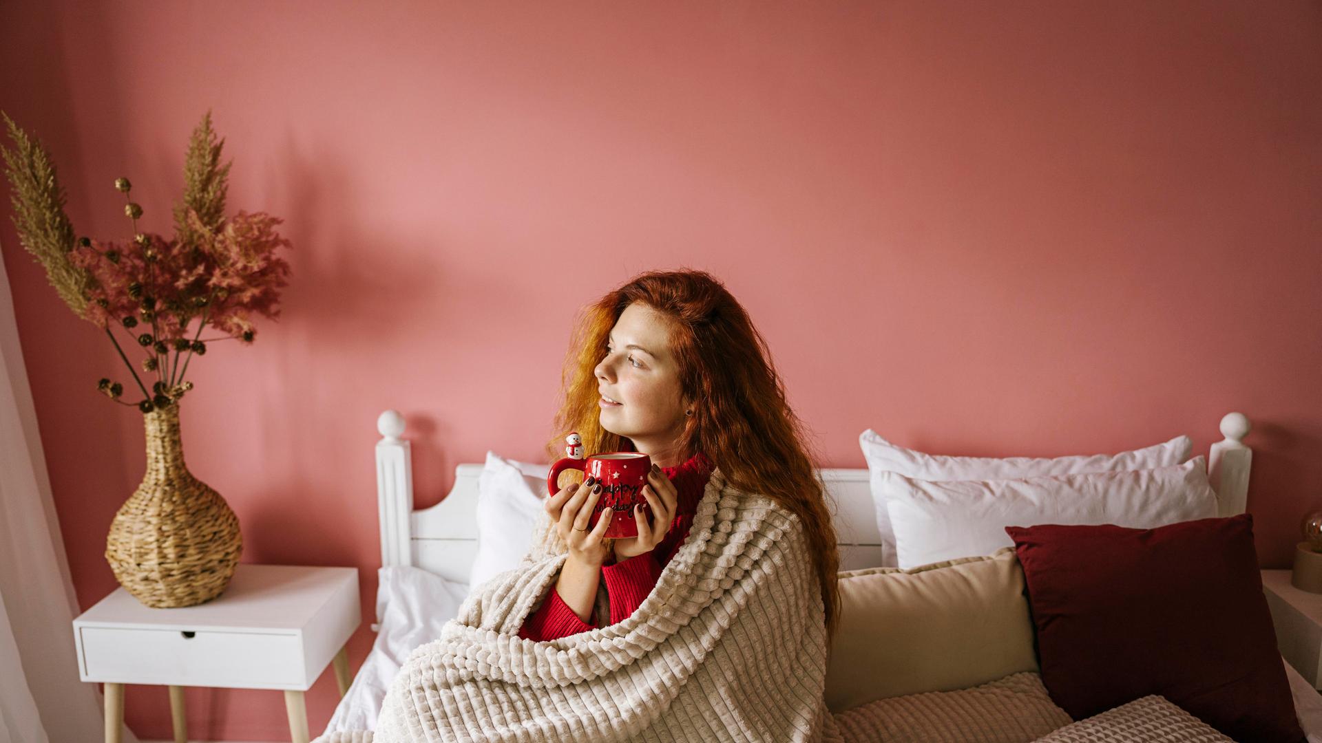 Eine Frau sitzt mit einer Tasse Kaffee auf ihrem Bett.