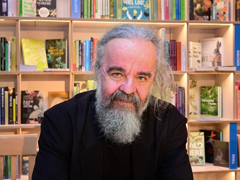 Der Schriftsteller Miljenko Jergović sitzt vor einem Bücherregal und schaut direkt in die Kamera.