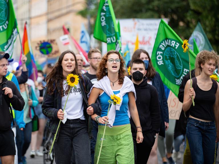 Zwei junge Frauen mit Sonnenblumen auf einer Demo. Im Hintergrund viele Fridays for Future-Fahnen.