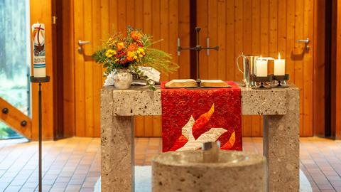 Innenraum einer Kirche mit einem Steinaltar in der Mitte, darauf eine aufgeschlagene Bibel, ein Kreuz, Blumen und Kerzen.