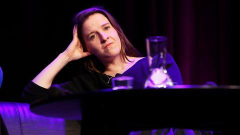 Helene Hegemann sitzt auf einer Bühne und blickt nachdenklich in die Kamera.