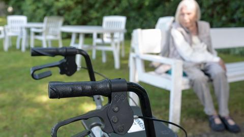 Ein Rollator im Vordergrund des Bildes, im Hintergrund, unscharf eine ältere Dame, vermutlich die Person, die auf diese Gehilfe angewiesen ist Ein Rollator im Vordergrund des Bildes, im Hintergrund, unscharf eine ältere Dame, vermutlich die Person, die auf diese Gehilfe angewiesen ist